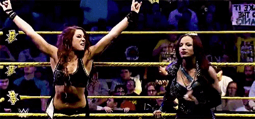 two female wrestlers are standing in a wrestling ring with their arms in the air .