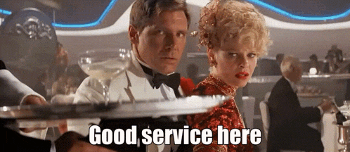 a man in a tuxedo is holding a tray in front of a woman who says good service here .