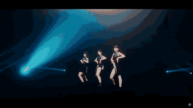 three women singing into microphones on a stage with a blue light behind them