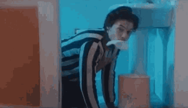 a man in a striped shirt is standing in a bathroom next to a sink .