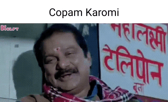 a man is sitting in front of a sign that says copam karom