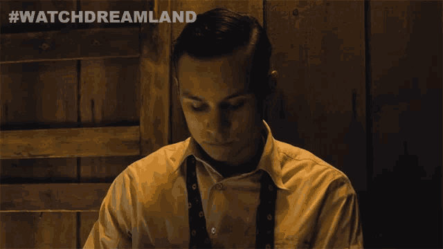 a man in a suit and tie is standing in front of a wooden wall with #watchdreamland on the bottom