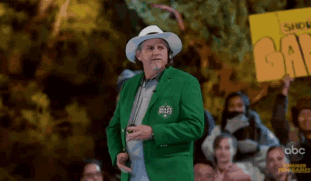 a man wearing a green jacket and a white hat is standing in front of a crowd holding a sign that says go
