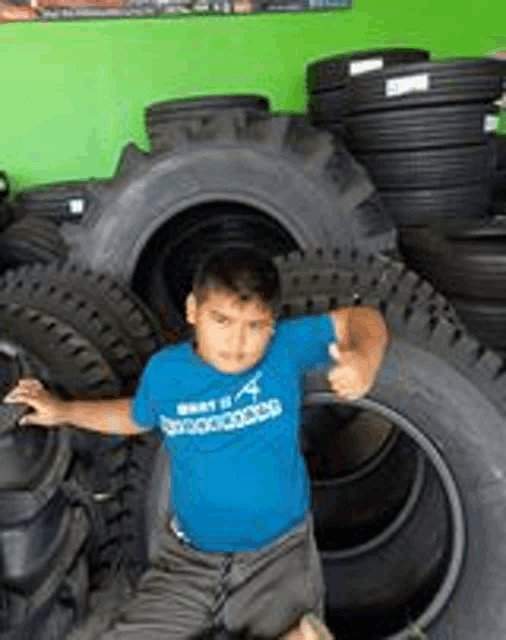 a young boy in a blue shirt is kneeling next to a pile of tires .