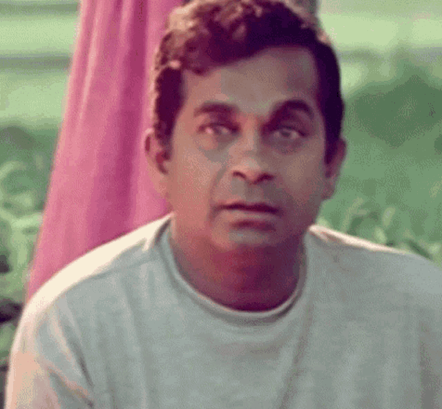 a man in a white shirt is sitting in front of a pink curtain .