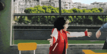 a girl in a red jacket is standing in front of a yellow chair