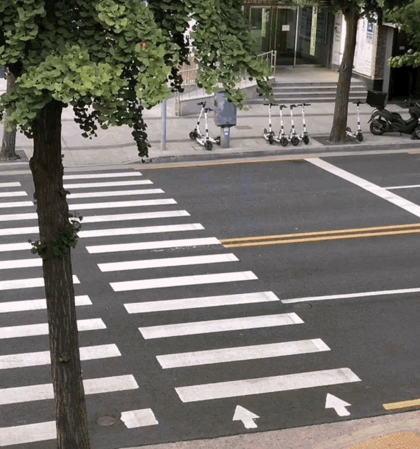 three scooters are parked on the side of the road near a crosswalk