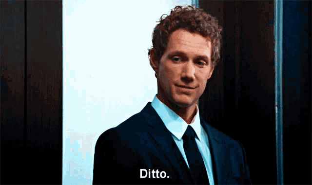 a man in a suit and tie says ditto in front of a door