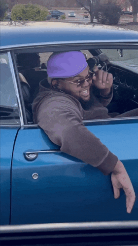 a man wearing a purple hat and sunglasses is sitting in a car
