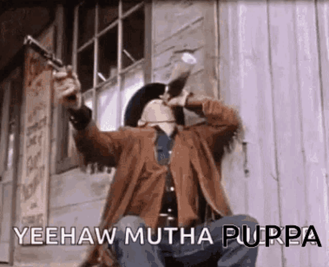 a man in a cowboy hat is sitting in front of a building holding a gun and saying yeehaw mutha purpa .