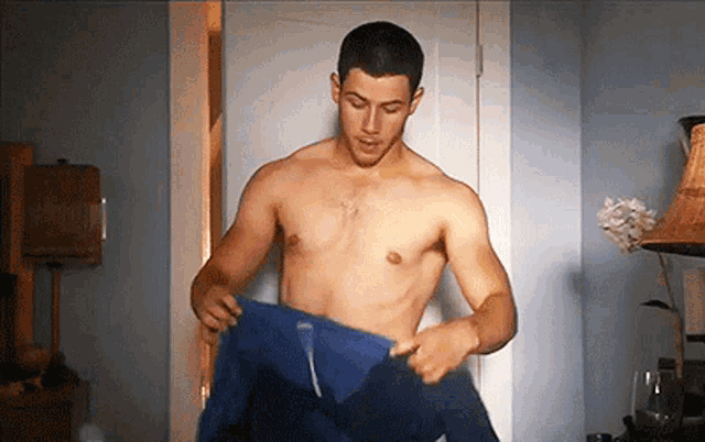 a shirtless man is taking off his blue shirt