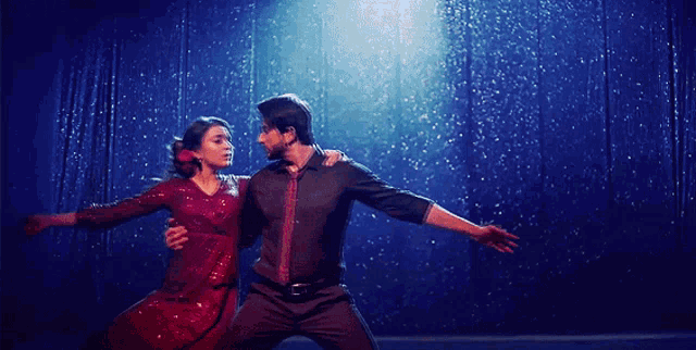 a man and woman are dancing on a stage in front of a blue curtain