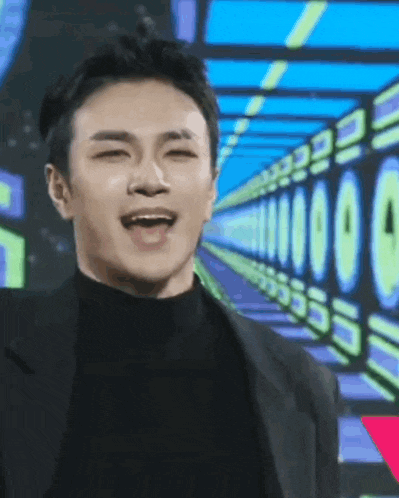 a man in a black suit and turtleneck is smiling in front of a row of numbers .