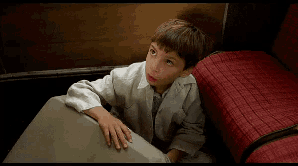 a young boy in a white shirt sits on a couch