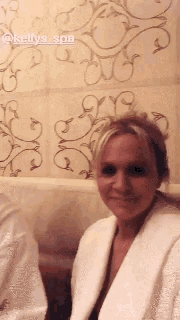 a woman in a white robe is standing in front of a wall that says kelly 's spa on it