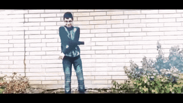 a man standing in front of a brick wall with his arms crossed