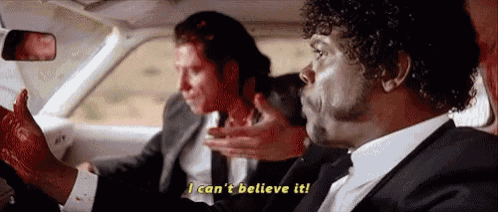a man in a suit and tie is driving a car while another man holds his hand to his face .