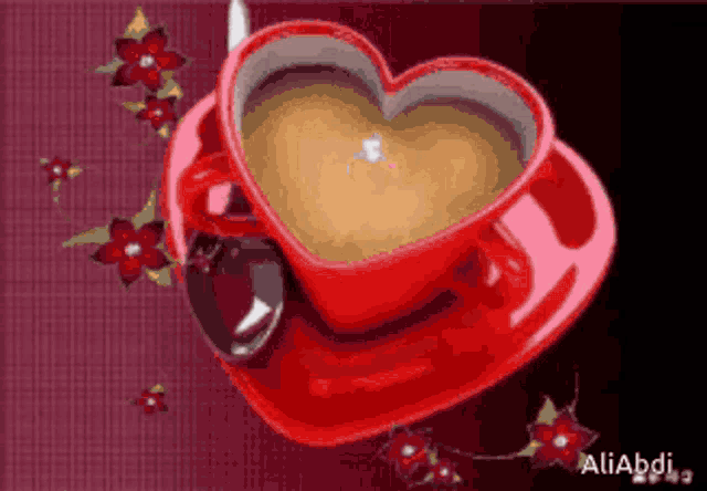 a red heart shaped cup of coffee with a spoon on a saucer