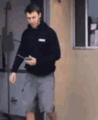a man in a black hoodie and gray shorts is walking down a sidewalk while looking at his phone .