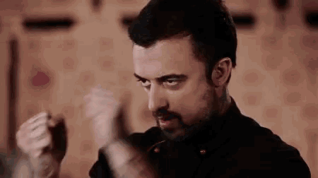 a man with a beard is holding a knife in his hand and making a fist .