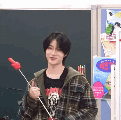 a young man in a plaid jacket is holding a red balloon in his hand .