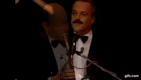 a man in a tuxedo is giving a speech in front of a microphone .