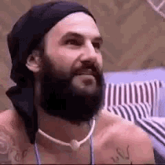 a man with a beard wearing a beanie and a necklace is sitting on a bed .