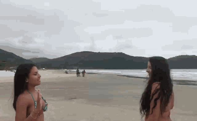 two women in bikinis are standing on a beach talking to each other .