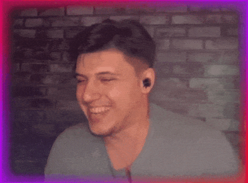 a man wearing earbuds smiles in front of a brick wall