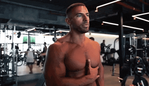 a shirtless man stands in a gym with his hands on his chest