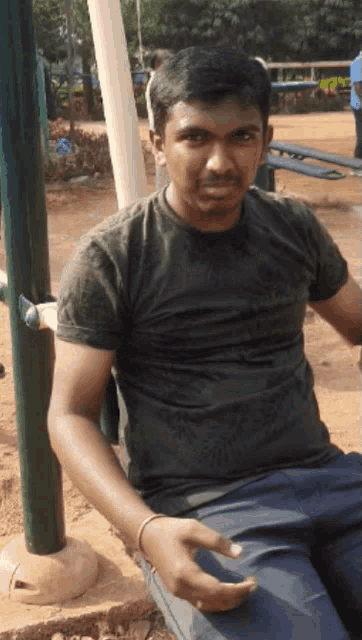 a man in a black shirt is sitting on a swing in a park