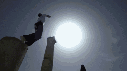 a man is jumping over a pillar with the sun behind him .