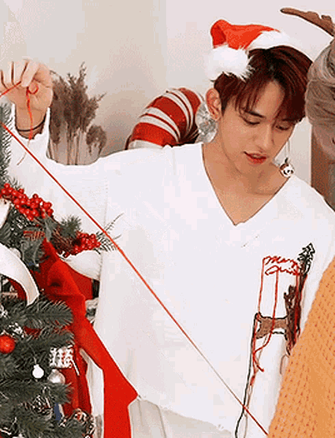 a man wearing a santa hat is decorating a christmas tree with a red string .