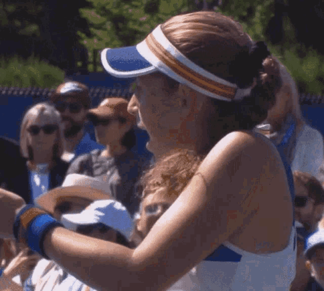 a woman wearing a blue and white visor is standing in front of a crowd of people .