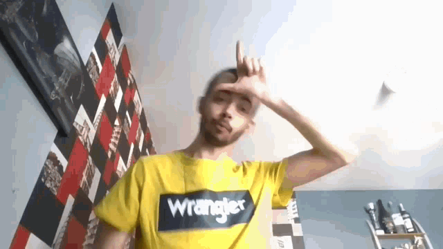 a man wearing a yellow wrangler t-shirt making a peace sign