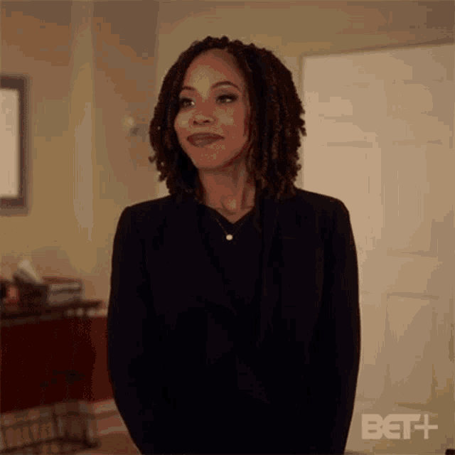 a woman with dreadlocks is wearing a black jacket and standing in a living room .
