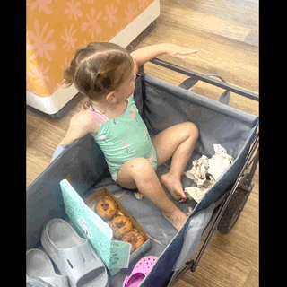 a little girl in a bathing suit sits in a wagon with a box of donuts
