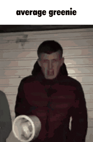 a man in a red jacket is holding a styrofoam cup in front of a garage door with the caption average greenie