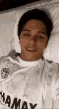 a man in a white shirt is laying on a bed with his eyes closed .