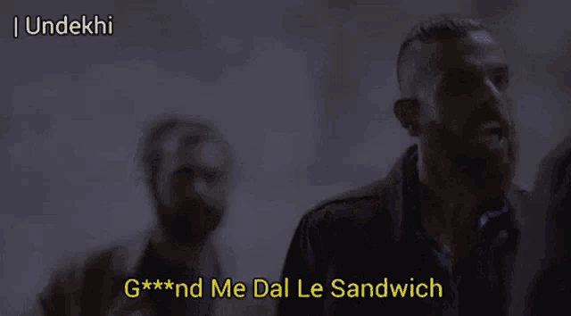 a man with a beard says " g *** nd me dal le sandwich " in a dark room