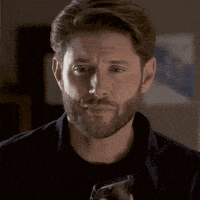 a man with a beard is holding a glass of wine and making a funny face .