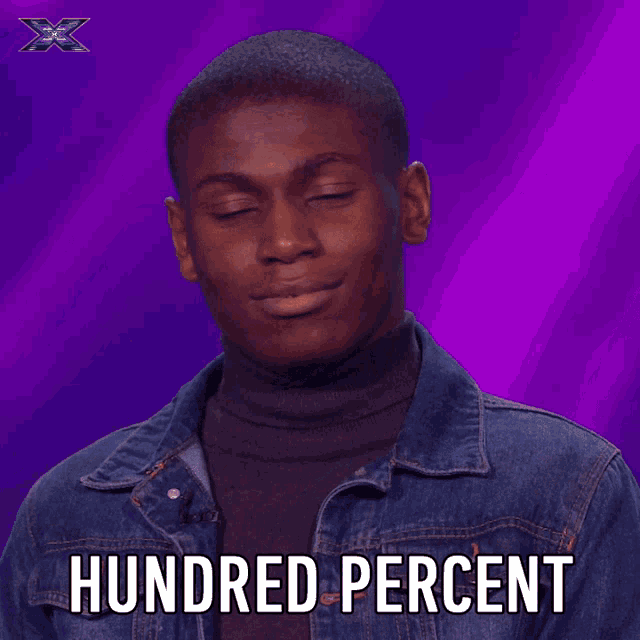a man in a denim jacket singing into a microphone with the words hundred percent above him