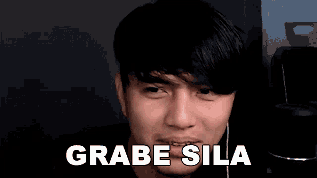 a young man is wearing headphones and making a funny face with the words grabe sila written above him .