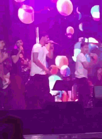 a man is singing into a microphone on a stage with purple lights behind him