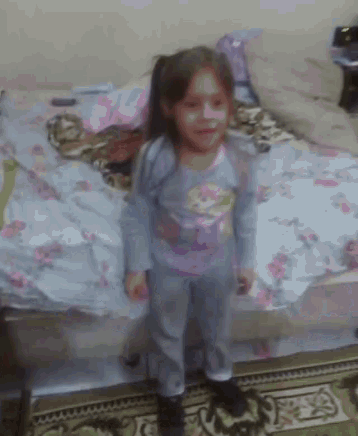 a little girl standing in front of a bed with a floral comforter