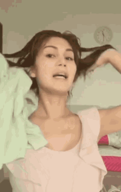 a woman in a pink top is holding her hair in front of a wall with a clock on it