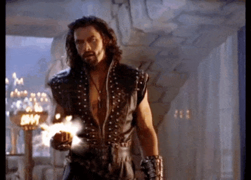 a man with long hair and a beard is wearing a leather vest and holding a torch .