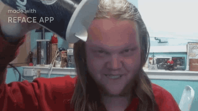a man with long hair and a red shirt is holding a can of soda in front of his head