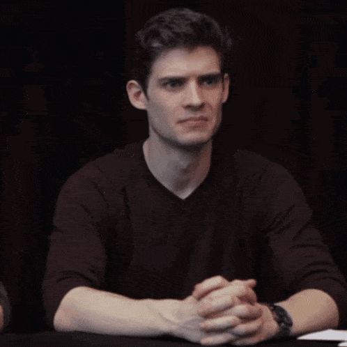 a young man is sitting at a table with his hand on his face and a watch on his wrist .