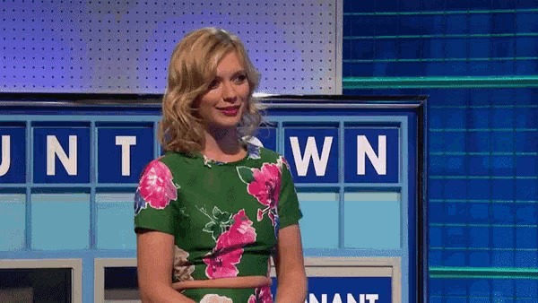 a woman in a green and pink floral dress is standing in front of a board with the letters unt and wn on it .